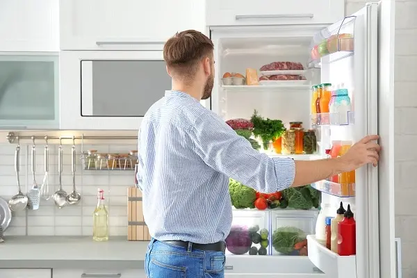 Man looking into an open refrigerator stocked with fresh food